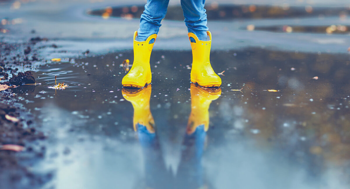 un enfant avec des bottes et un ciré jaune, les pieds dans l'eau