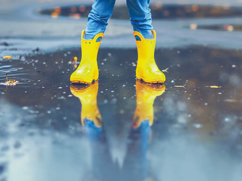 un enfant avec des bottes et un ciré jaune, les pieds dans l'eau