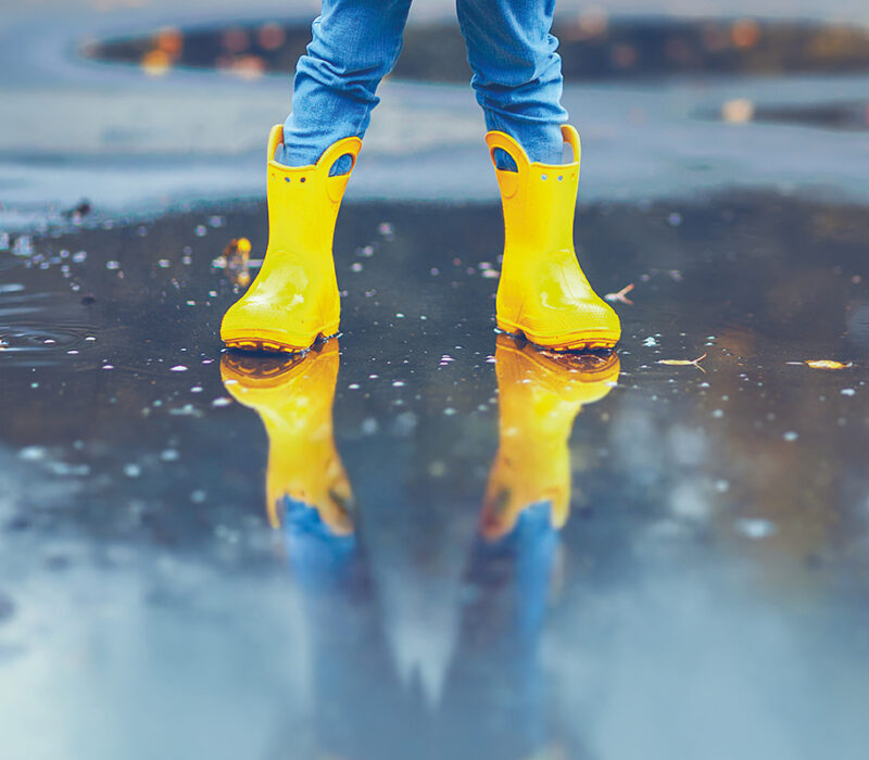 un enfant avec des bottes et un ciré jaune, les pieds dans l'eau